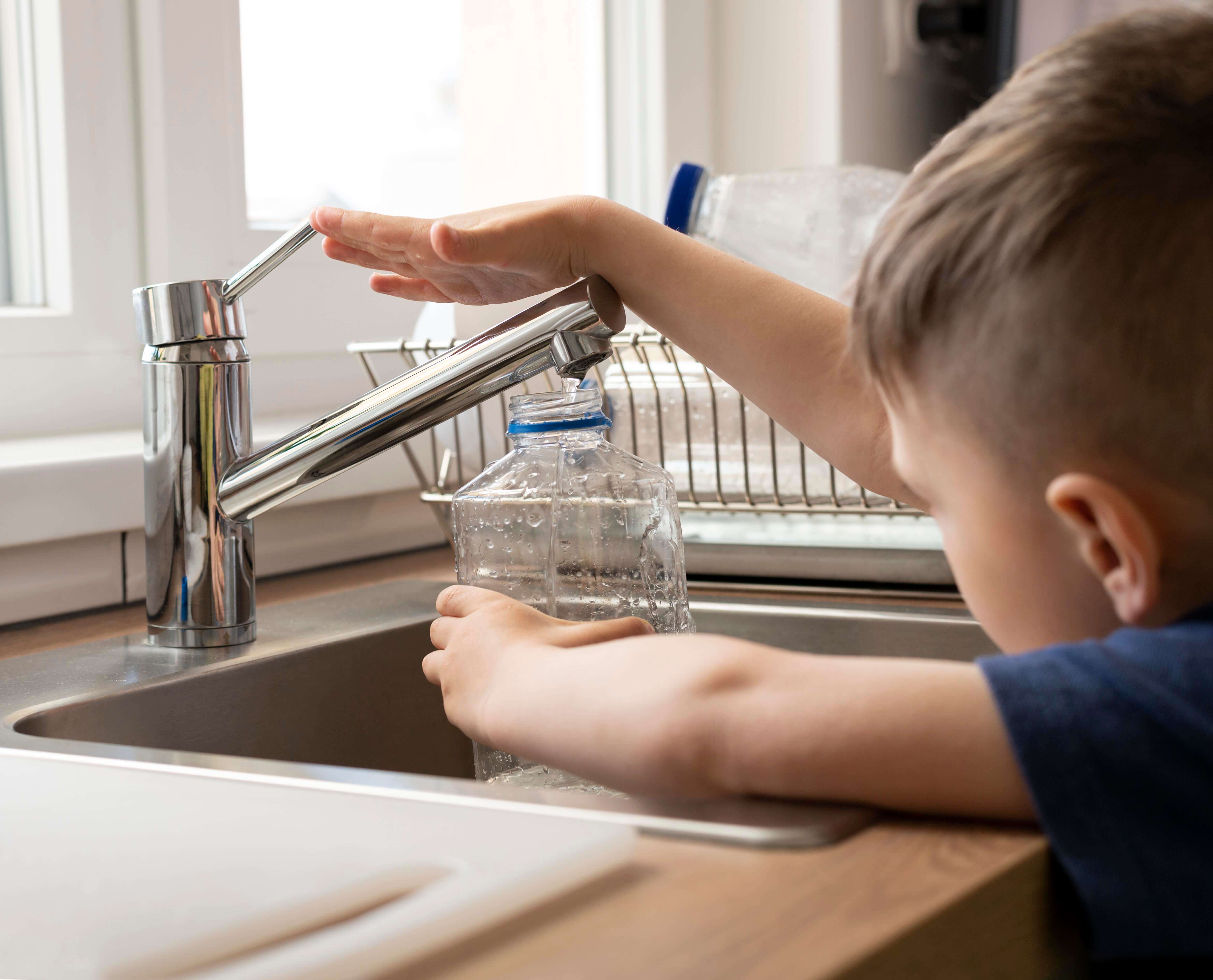 Kind füllt Trinkflasche am Wasserhahn – sicheres Leitungswasser im Alltag.